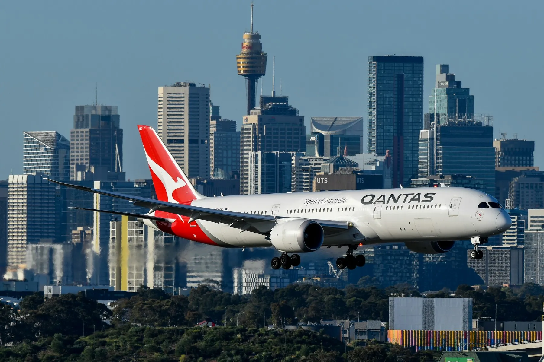 A Qantas jet on approach to Sydney Airport with the Sydney skyline behind it